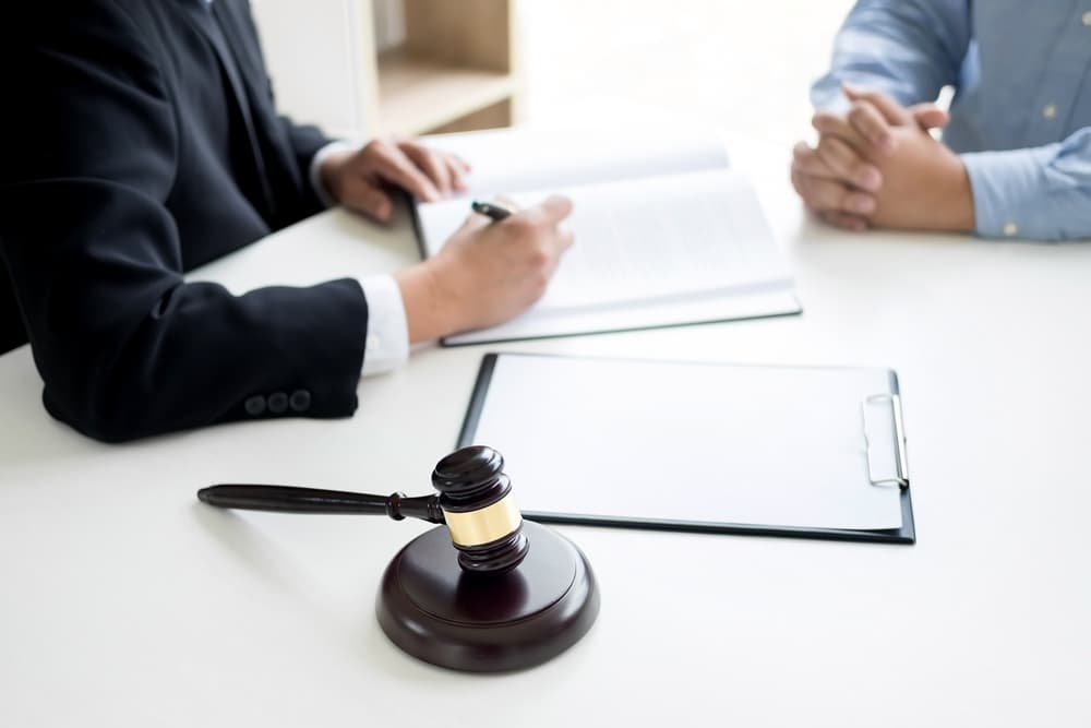 A lawyer and client discuss a case at a desk with legal documents and a gavel.