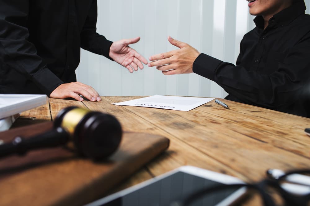 Two people shaking hands over a signed contract at a wooden table with a gavel.