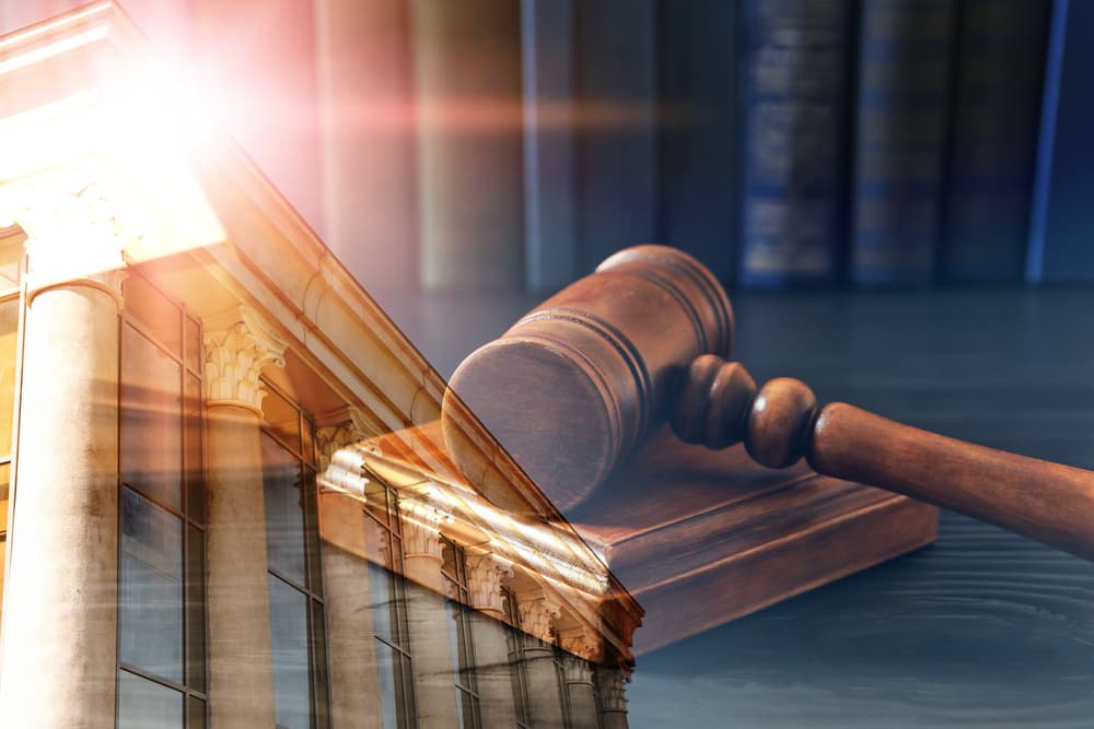 A gavel on a desk is overlaid with an image of courthouse pillars in sunlight.