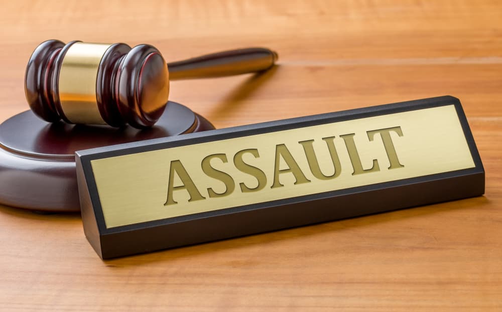 A gavel rests beside a plaque labeled "ASSAULT" on a wooden courtroom desk.