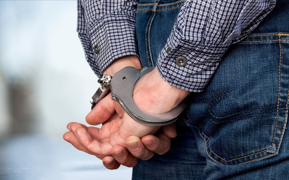 A person wearing a plaid shirt and jeans is handcuffed with hands behind their back.