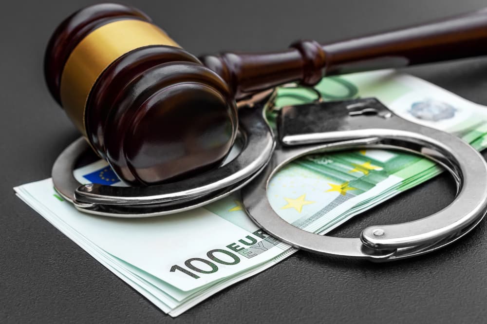 Gavel, handcuffs, and stack of euro banknotes on a black surface, representing legal and financial issues.