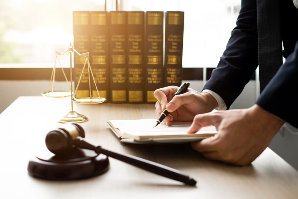 Lawyer writing on a notepad at a desk with a gavel, scales, and law books.