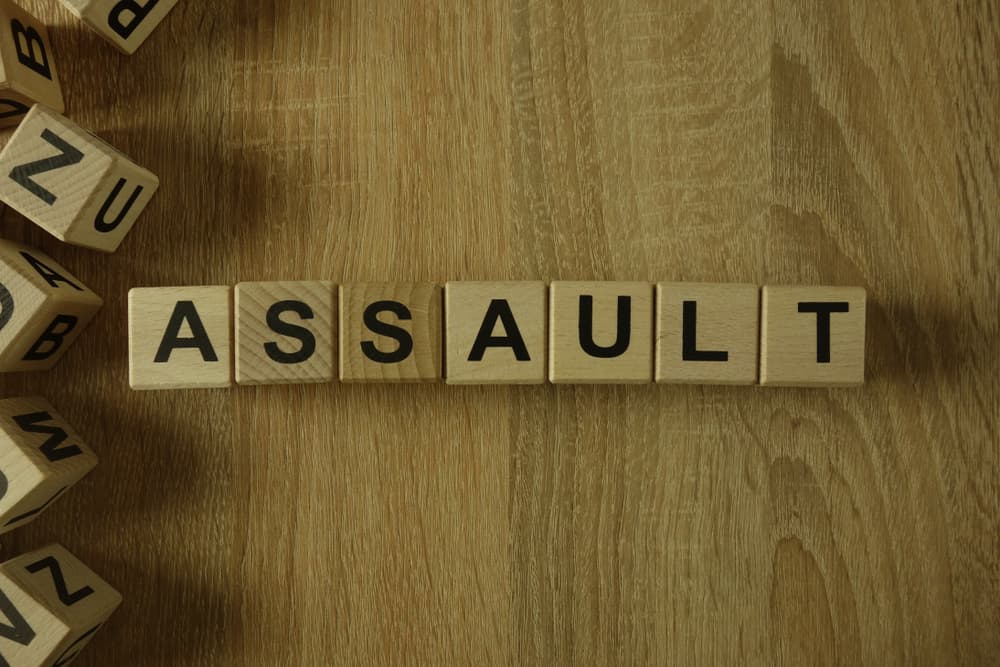 Wooden blocks spell out the word "ASSAULT" on a wooden surface, with scattered blocks nearby.