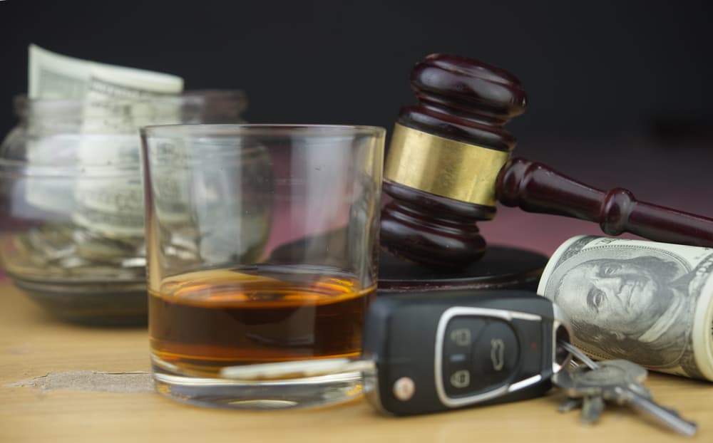 A glass of whiskey, car keys, a gavel, and a jar of money are displayed.