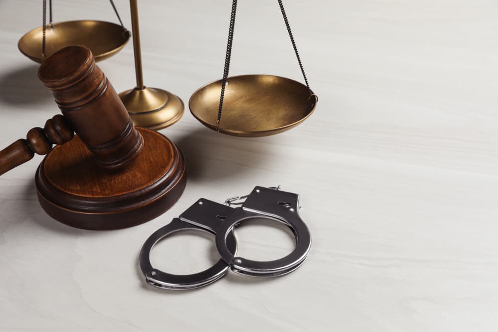 A gavel, scales of justice, and handcuffs are placed on a white marble surface.